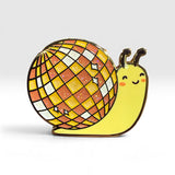 A cute enamel pin shaped like a yellow snail with a disco ball shell, set against a clean white background.