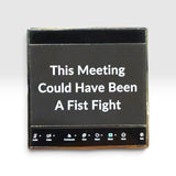 A square black enamel pin with a gold-toned metal border and a black magnetic backing. The front features white text that reads 'This Meeting Could Have Been A Fist Fight' with various meeting app icons along the bottom edge, set against a plain light gray background.