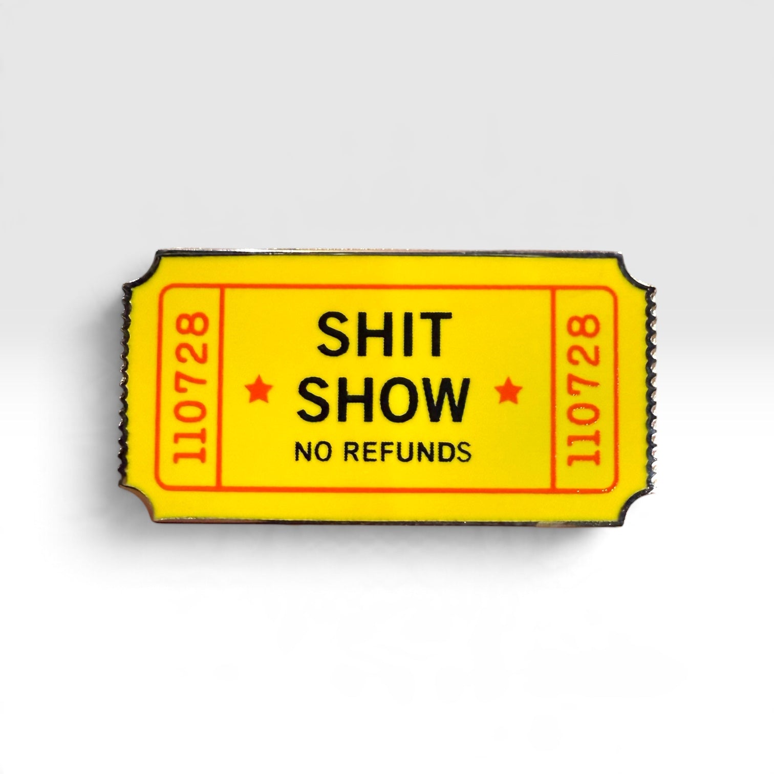 A novelty enamel pin shaped like a yellow movie ticket with the text 'SHIT SHOW NO REFUNDS' and red serial numbers, shown on a light gray background.