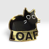A black cat-shaped enamel pin with gold trim and the word 'LOAF' in black on a gold banner below, shown on a light gray background.