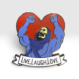 An enamel pin featuring a cartoon skeleton with raised fists in front of a red glitter heart, with a white banner below reading 'LIVE.LAUGH.LOVE.'