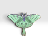 A luna moth enamel pin with light green wings, a purple thorax, and silver metal outlines, shown on a light gray gradient background.