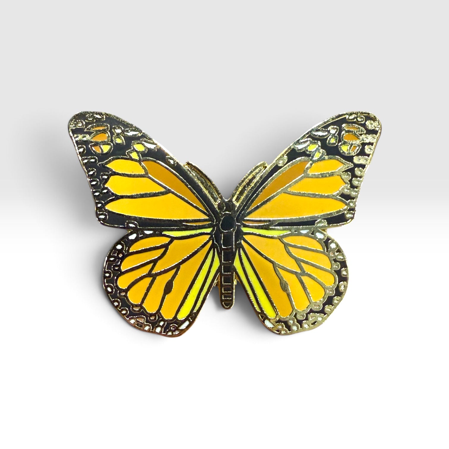 A butterfly-shaped pin with vibrant yellow wings outlined in black and detailed with metallic gold-toned patterns, set against a clean light gray background.