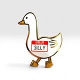 A white goose-shaped enamel pin with gold metal outlines, featuring a red and white 'HELLO MY NAME IS SILLY' name tag on its side, set against a clean light gray background.