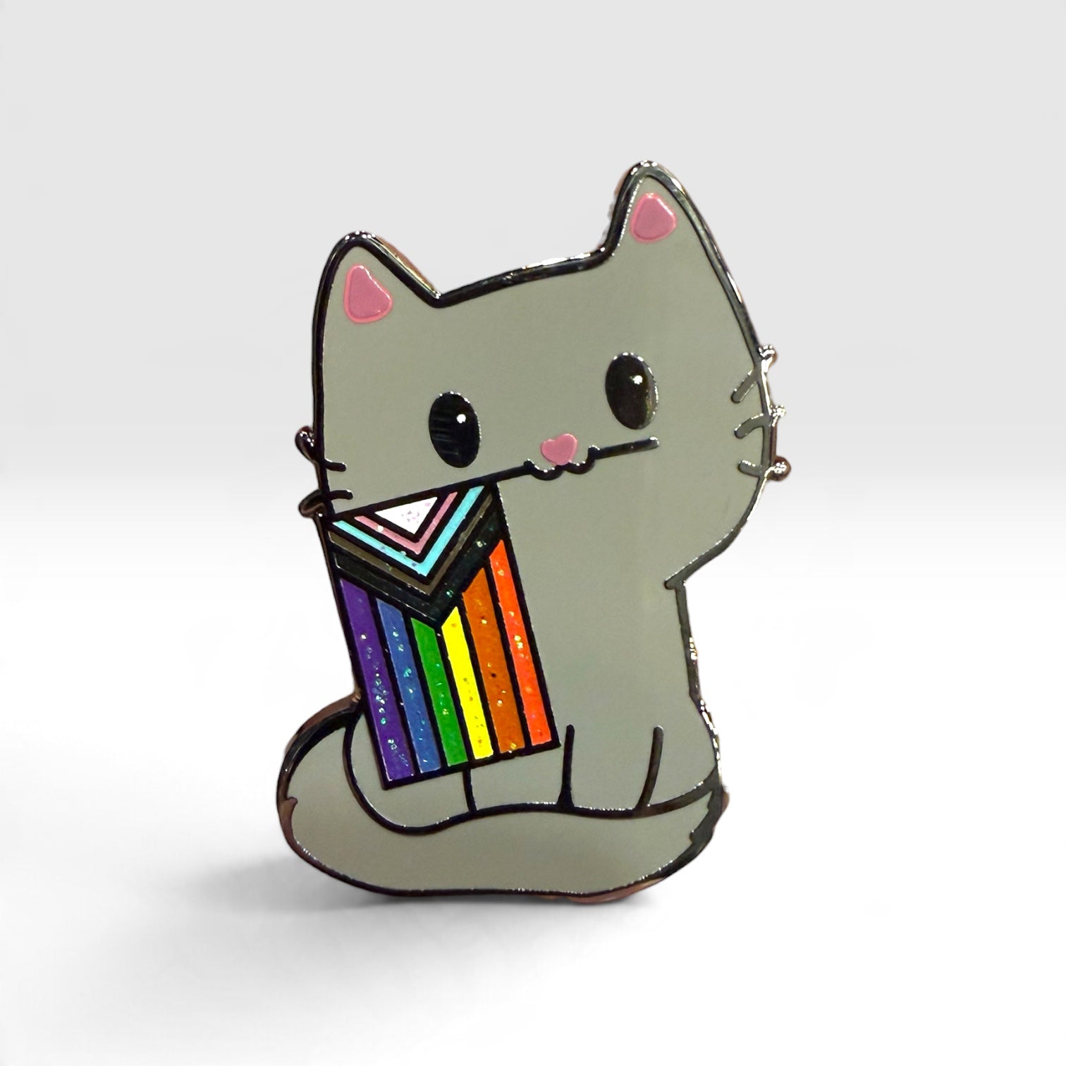 A gray cat enamel pin holding a rainbow-striped flag, shown on a clean light gray background.