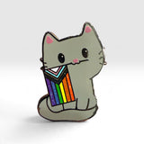 A gray cat enamel pin holding a rainbow-striped flag, shown on a clean light gray background.