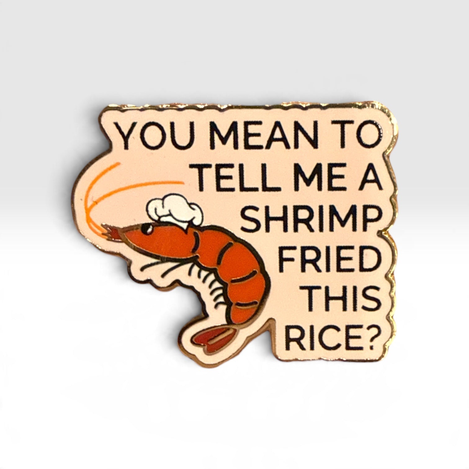 A novelty enamel pin shaped like a shrimp with a chef's hat, featuring the text 'YOU MEAN TO TELL ME A SHRIMP FRIED THIS RICE?' in black lettering on a light beige background with a gold-toned outline.