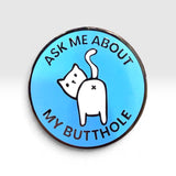 A round enamel pin with a light blue background, featuring a white cartoon cat with its back turned and the text 'ASK ME ABOUT MY BUTTHOLE' in black lettering.