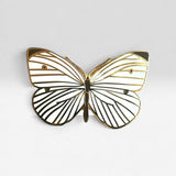 A butterfly-shaped pin with white enamel wings outlined in gold and black striped detailing, shown against a light gray background.