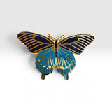 A butterfly-shaped enamel pin with gold metal outlines, featuring a dark navy blue upper wing section and a bright teal-blue lower wing section with gold vein details.