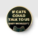 A round enamel pin with a black face, gold border, and gold lettering that reads 'IF CATS COULD TALK TO US THEY WOULDN'T', with a cat silhouette at the bottom, shown on a light gray background.
