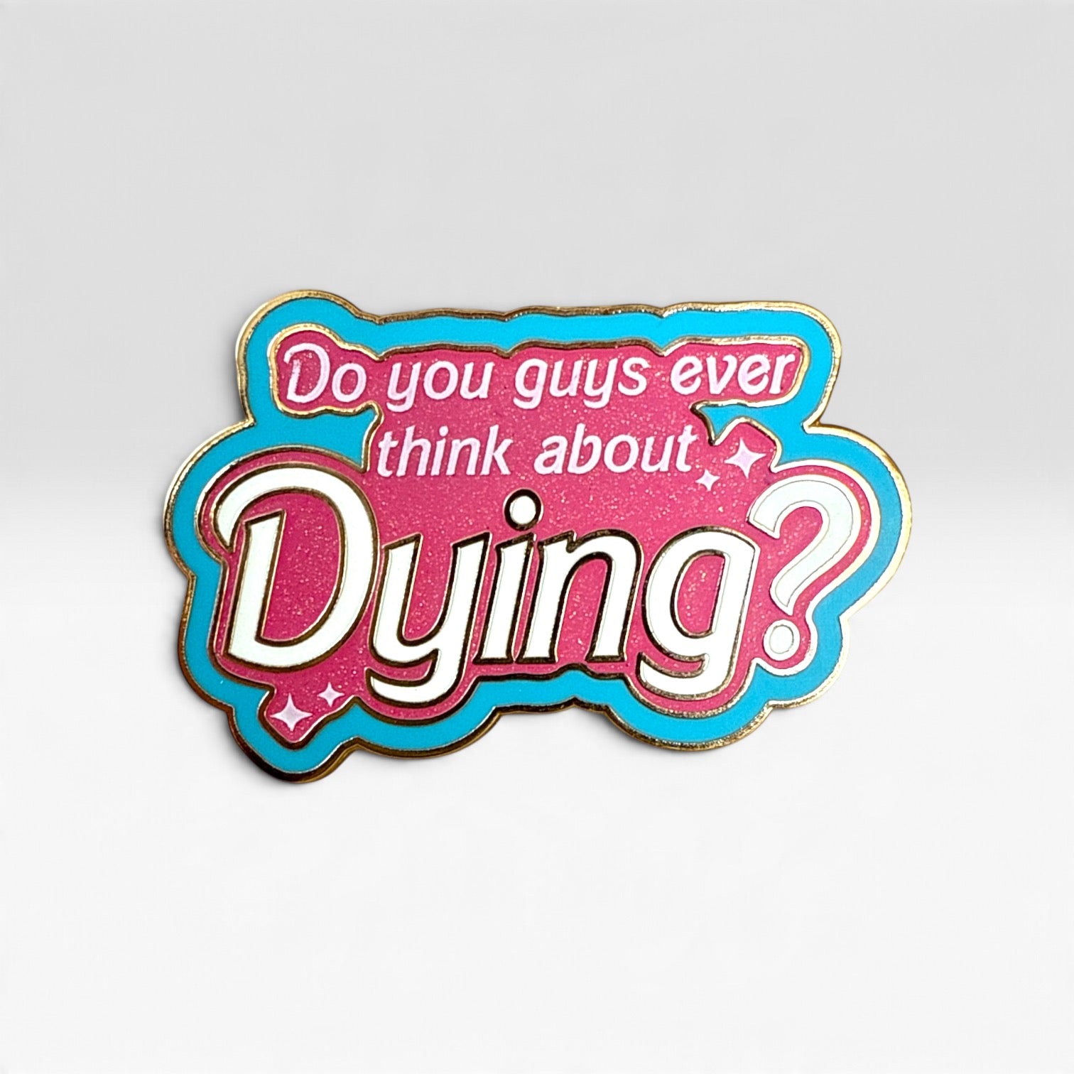 A die-cut enamel pin with the text 'Do you guys ever think about Dying?' in white lettering. The design features a bright pink glittery fill, a vibrant turquoise blue border, and a thin gold metal outline, set against a clean light gray background.