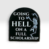 A tombstone-shaped black enamel pin featuring white text that reads 'GOING TO HELL ON A FULL SCHOLARSHIP' and a white skeleton dancing on the right side, shown against a light gray gradient background.