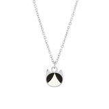 A silver chain necklace featuring a minimalist pendant shaped like a cat's head, detailed with black and white enamel sections, set against a plain white background.