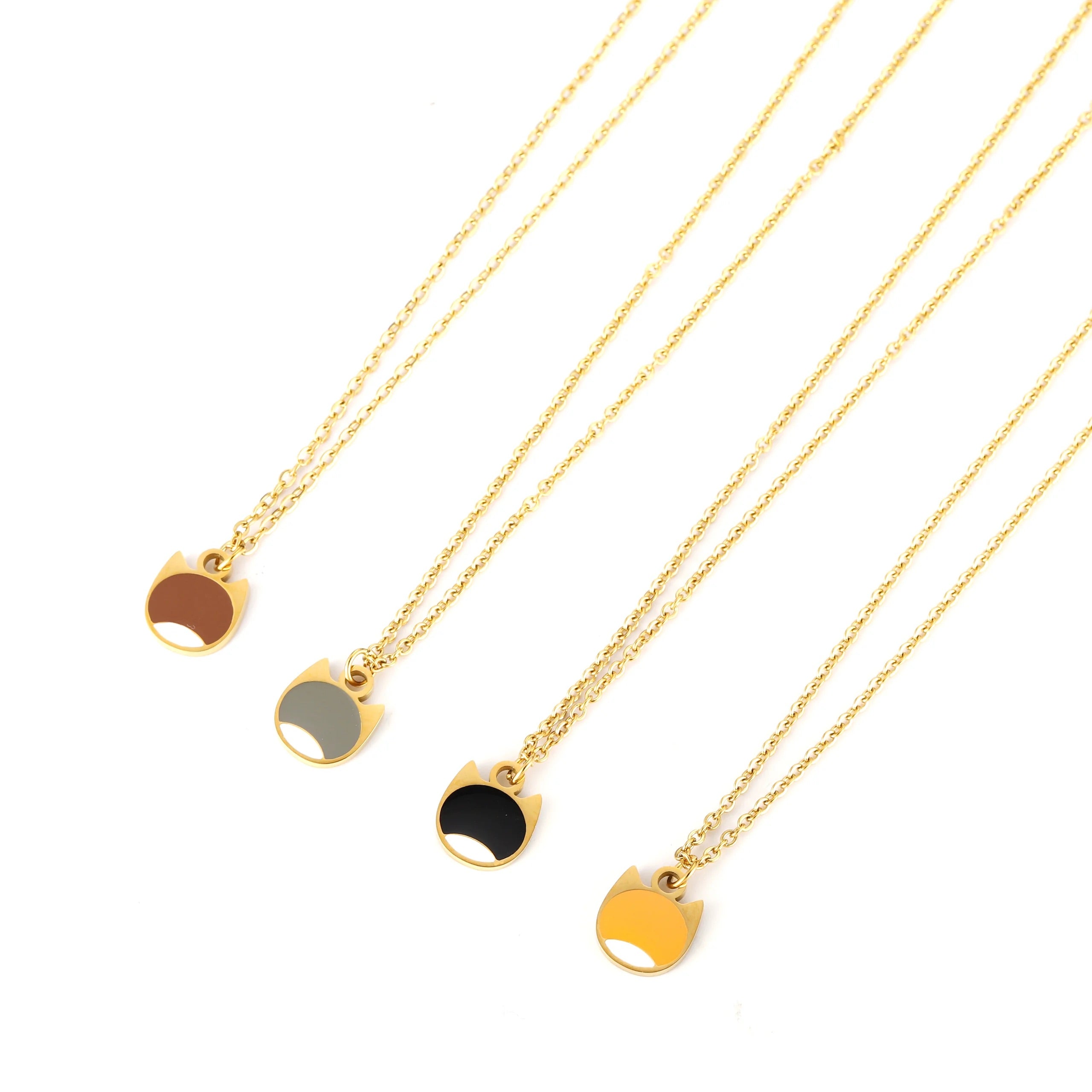 Four gold-tone cat-shaped pendant necklaces with different colored paws (brown, gray, black, and yellow) arranged diagonally on a white background.