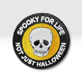 A circular embroidered patch featuring a white skull on a yellow background, surrounded by a black border with the text 'SPOOKY FOR LIFE NOT JUST HALLOWEEN' in white.